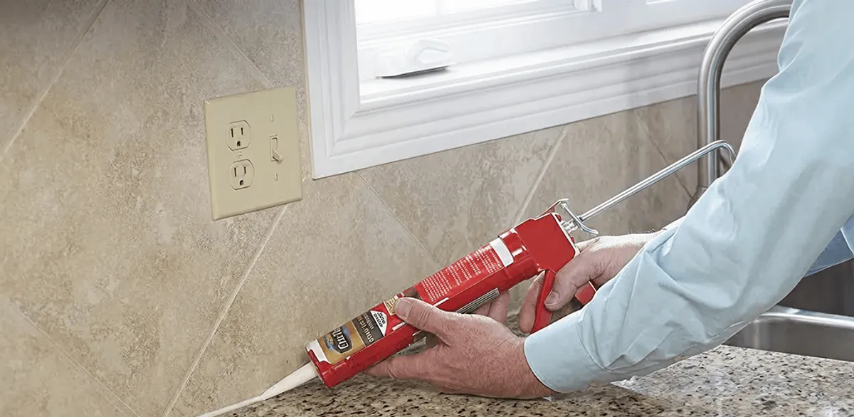 Handyman applying caulk along a kitchen backsplash and countertop seam in Naperville, IL